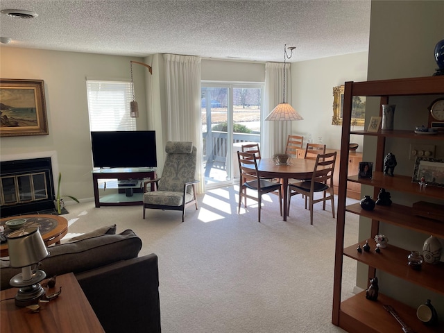 carpeted living area with visible vents, a textured ceiling, a healthy amount of sunlight, and a glass covered fireplace