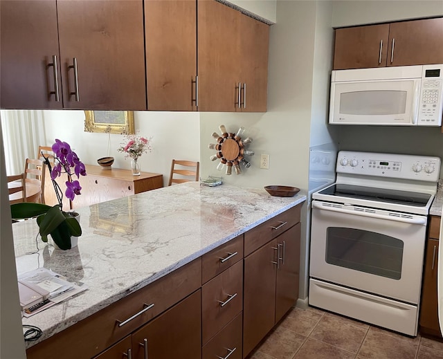 kitchen featuring tile patterned floors, white appliances, and light stone countertops