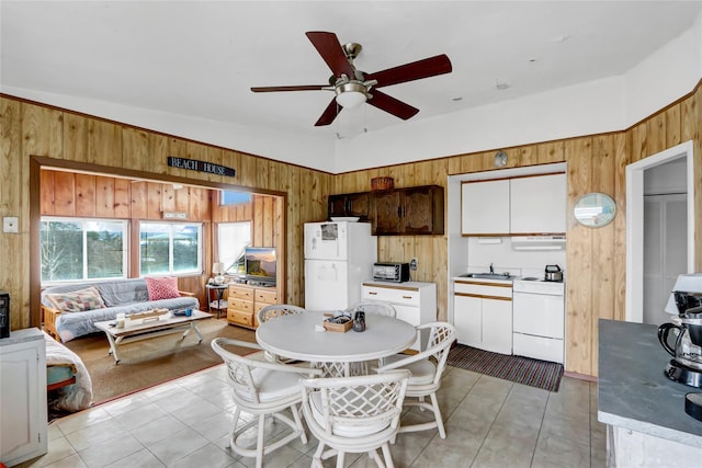 interior space with wooden walls, ceiling fan, light tile patterned flooring, white appliances, and a sink