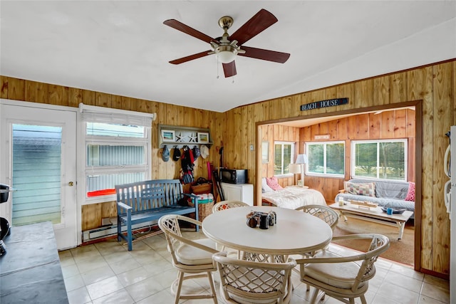 dining room with ceiling fan, lofted ceiling, wood walls, and light tile patterned floors