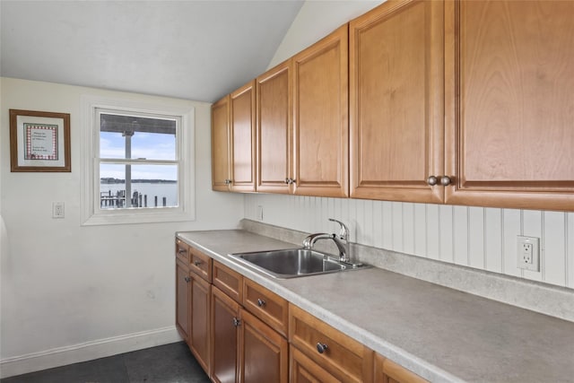 kitchen with baseboards, lofted ceiling, a sink, light countertops, and brown cabinets