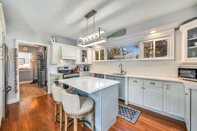 kitchen with dark wood finished floors, light countertops, glass insert cabinets, appliances with stainless steel finishes, and a kitchen bar