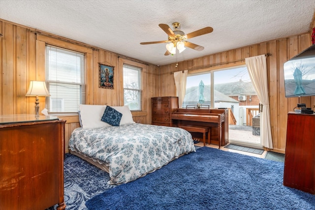 carpeted bedroom featuring a textured ceiling, wooden walls, and access to outside