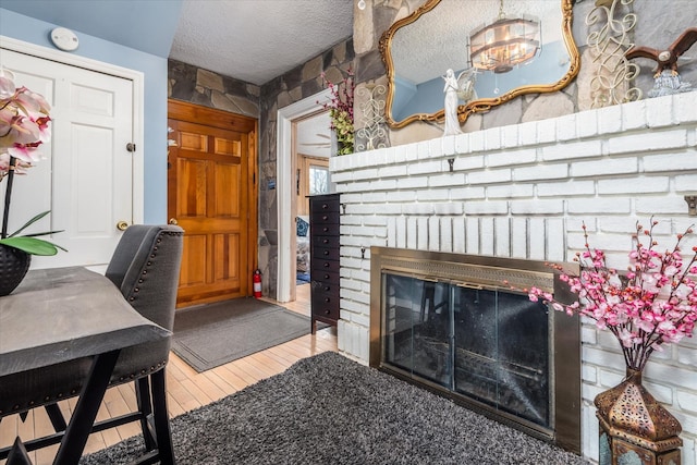 living room with a brick fireplace, a textured ceiling, and wood finished floors