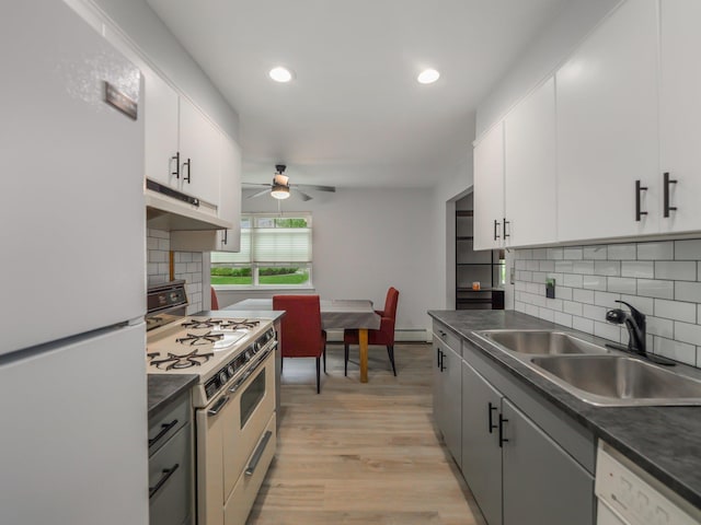 kitchen with white appliances, under cabinet range hood, a sink, a ceiling fan, and dark countertops