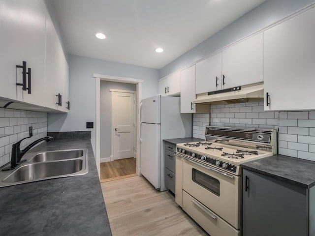 kitchen featuring under cabinet range hood, white appliances, a sink, dark countertops, and recessed lighting