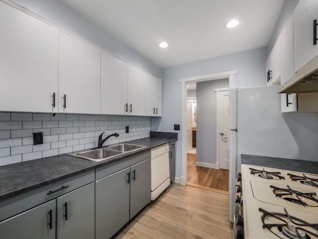 kitchen with white dishwasher, a sink, light wood-type flooring, gas range oven, and dark countertops