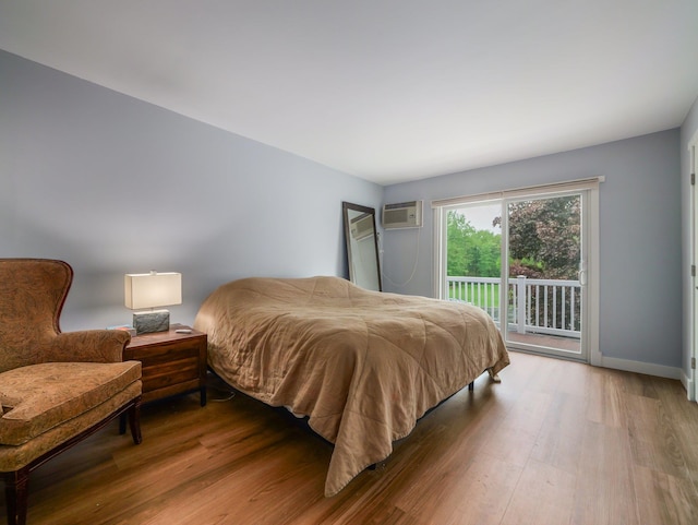 bedroom with access to exterior, wood finished floors, a wall unit AC, and baseboards