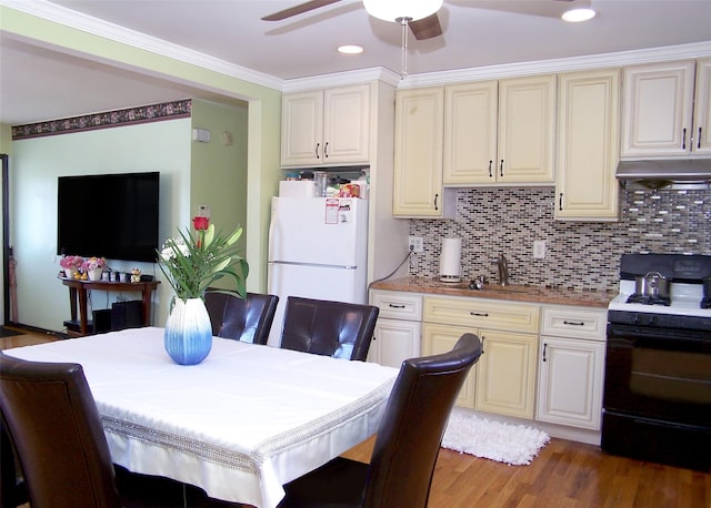 kitchen with crown molding, under cabinet range hood, decorative backsplash, freestanding refrigerator, and gas stove