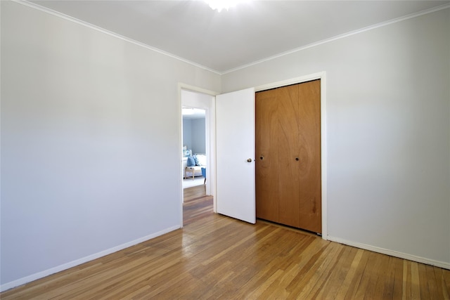 unfurnished bedroom with a closet, baseboards, wood finished floors, and crown molding