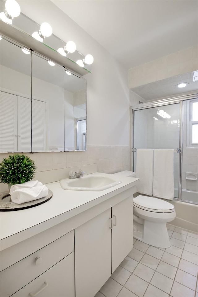 bathroom featuring tile patterned flooring, toilet, vanity, combined bath / shower with glass door, and tile walls