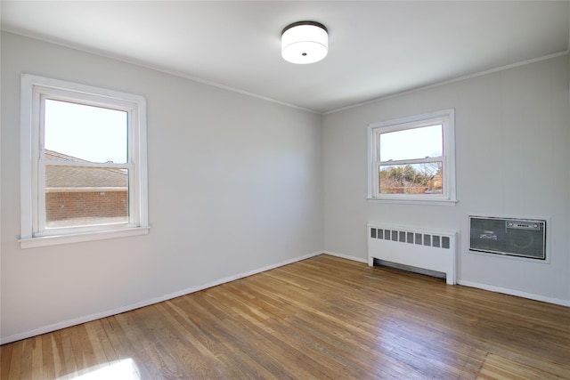 unfurnished room with a wall unit AC, radiator, baseboards, wood-type flooring, and crown molding