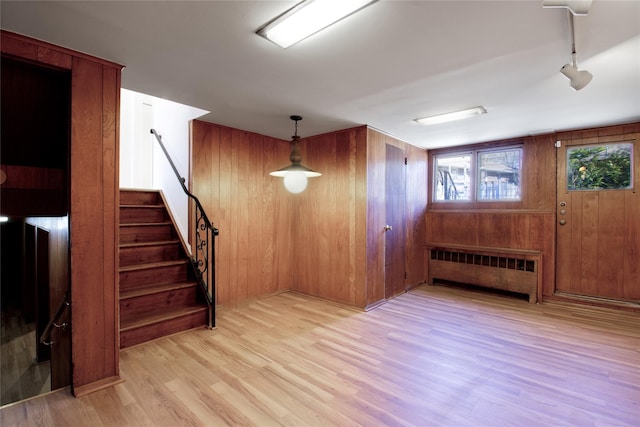 interior space with wooden walls, wood finished floors, radiator heating unit, stairs, and track lighting