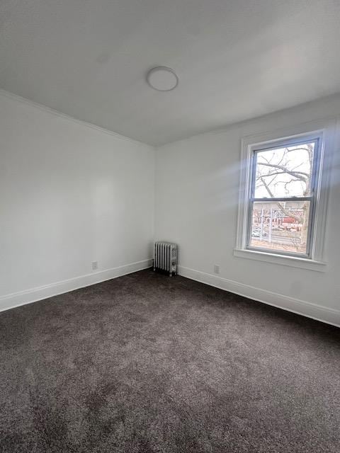 empty room with radiator heating unit, baseboards, and dark colored carpet