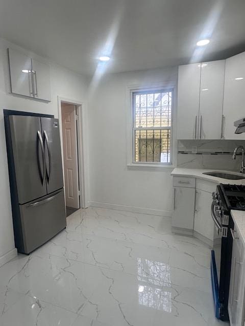 kitchen featuring black range with gas stovetop, freestanding refrigerator, marble finish floor, white cabinetry, and a sink