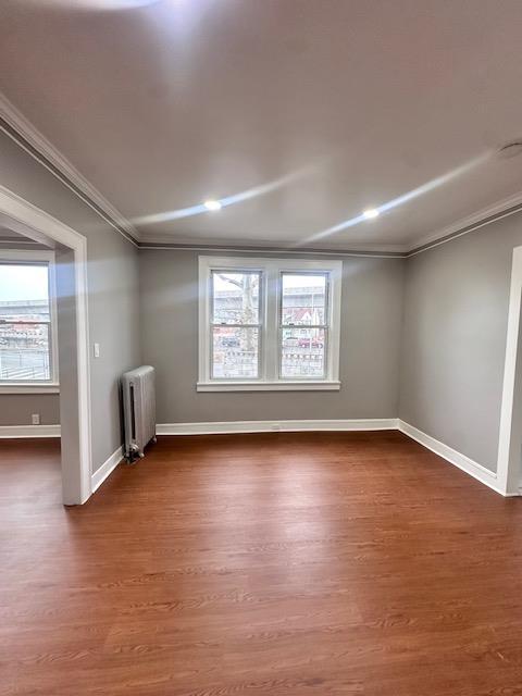 unfurnished room with radiator, dark wood-type flooring, baseboards, and ornamental molding