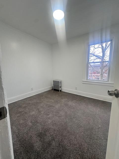 empty room featuring radiator heating unit, baseboards, and dark colored carpet