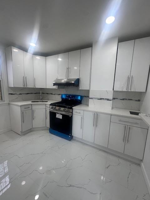 kitchen featuring a sink, light countertops, under cabinet range hood, stainless steel gas range oven, and marble finish floor