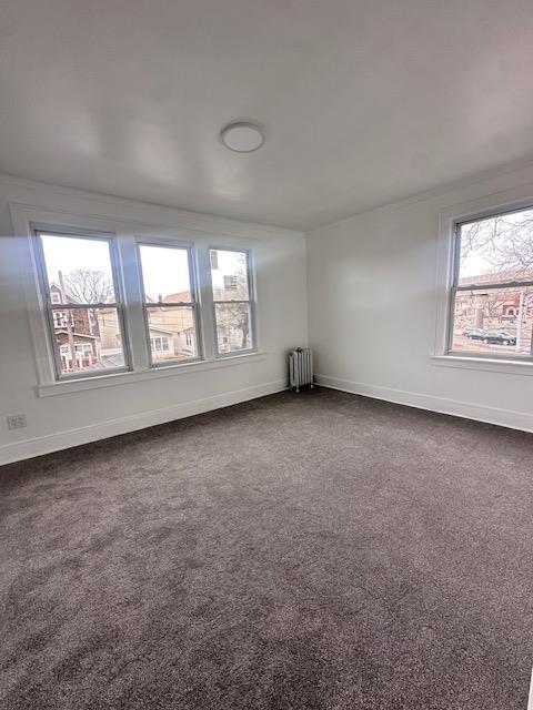 spare room with dark carpet, plenty of natural light, and radiator heating unit