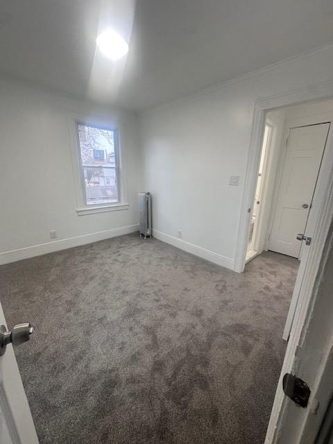 carpeted spare room featuring radiator and baseboards