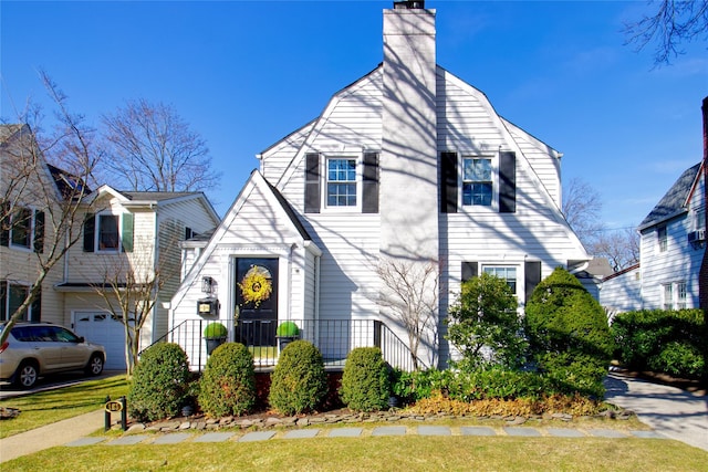 view of front of home with a gambrel roof, an attached garage, and a chimney