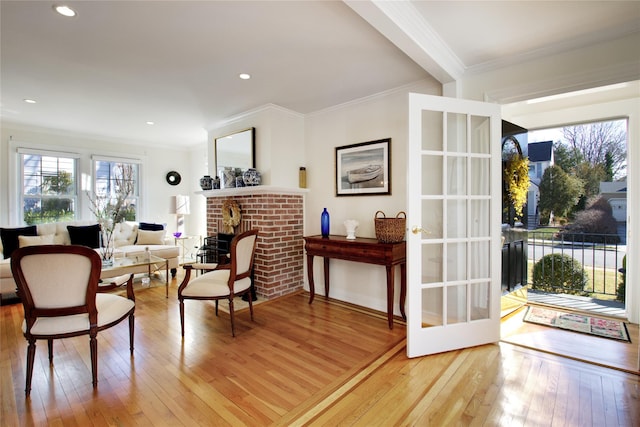 sitting room with a brick fireplace, light wood-type flooring, and ornamental molding