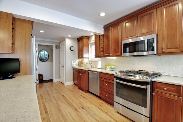 kitchen featuring light stone counters, light wood finished floors, a sink, decorative backsplash, and stainless steel appliances