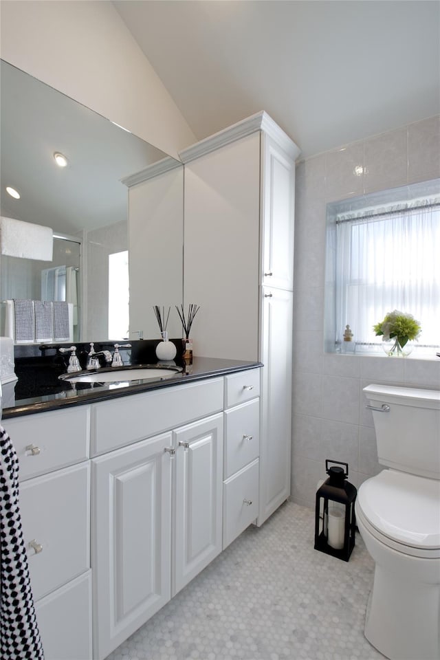 bathroom with a shower with door, toilet, vanity, vaulted ceiling, and tile walls