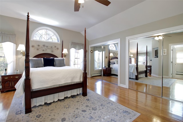 bedroom featuring two closets, a ceiling fan, wood finished floors, a baseboard radiator, and vaulted ceiling