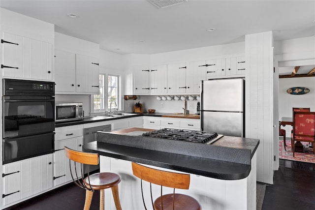 kitchen featuring dark countertops, stainless steel appliances, white cabinetry, a warming drawer, and a sink