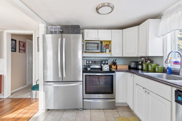 kitchen with light tile patterned floors, a sink, white cabinets, appliances with stainless steel finishes, and dark countertops