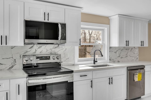 kitchen featuring light stone counters, a sink, decorative backsplash, stainless steel appliances, and white cabinetry