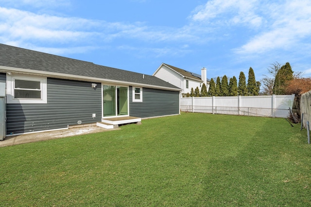 rear view of house featuring a lawn, a shingled roof, and a fenced backyard