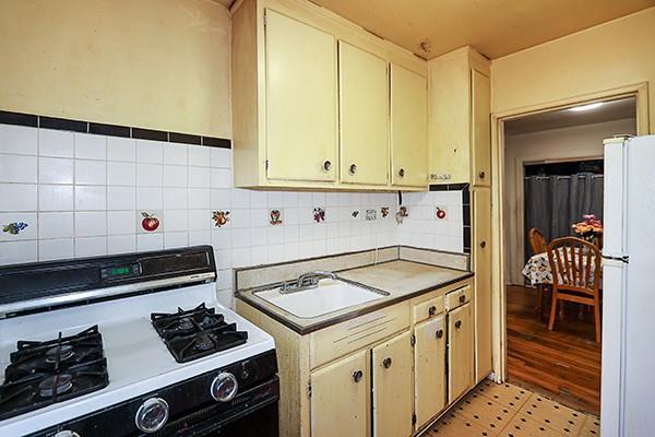 kitchen featuring a sink, tasteful backsplash, gas range oven, freestanding refrigerator, and light floors