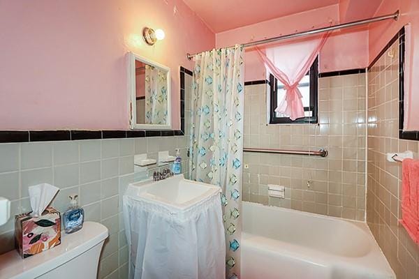 bathroom featuring shower / bath combination with curtain, toilet, tile walls, and a sink