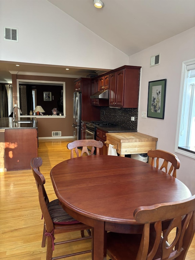 dining area featuring visible vents, light wood-style floors, and vaulted ceiling