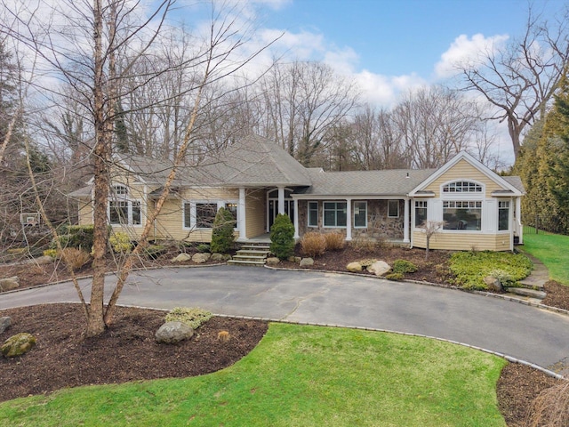 view of front of house featuring aphalt driveway, a front lawn, and a shingled roof