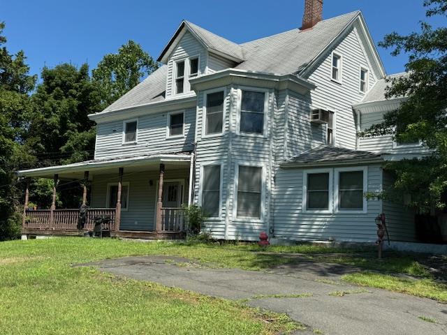 view of front of home featuring a front yard, covered porch, and a chimney