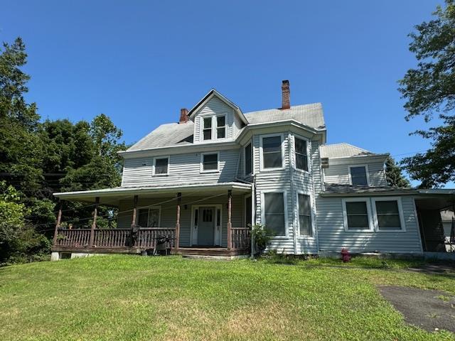 view of front of property with a carport, covered porch, a chimney, and a front lawn