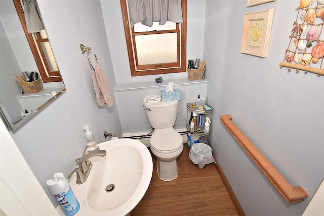 half bath with toilet, wood finished floors, baseboards, and a sink