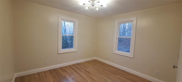 spare room featuring a chandelier, light wood finished floors, baseboards, and visible vents