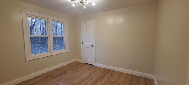 empty room with a chandelier, light wood finished floors, and baseboards