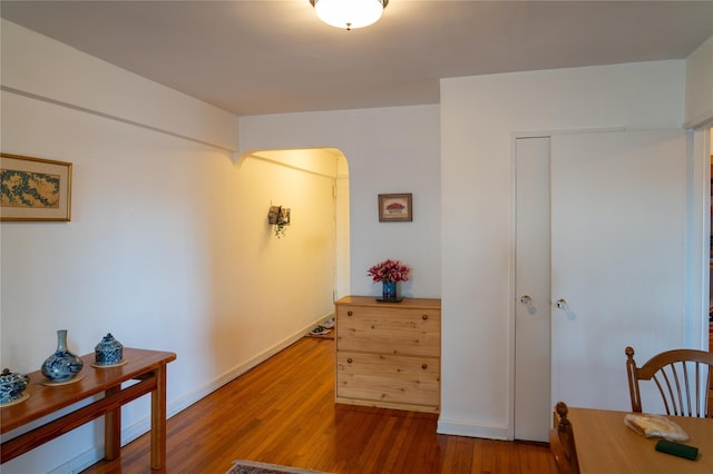 hallway featuring wood finished floors, baseboards, and arched walkways