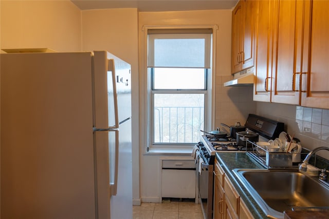 kitchen with under cabinet range hood, decorative backsplash, freestanding refrigerator, stainless steel gas stove, and a sink