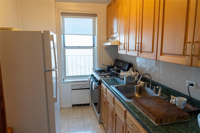 kitchen with freestanding refrigerator, a sink, under cabinet range hood, stainless steel gas range oven, and dark countertops