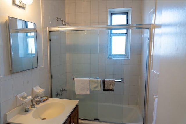 full bath featuring vanity, tile walls, and combined bath / shower with glass door