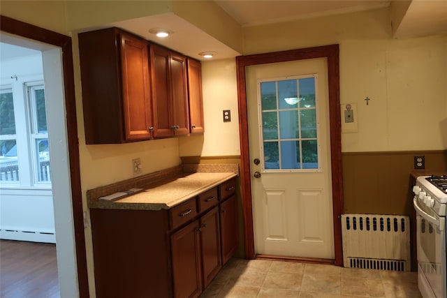 kitchen featuring a baseboard heating unit, radiator, a wainscoted wall, and white gas stove