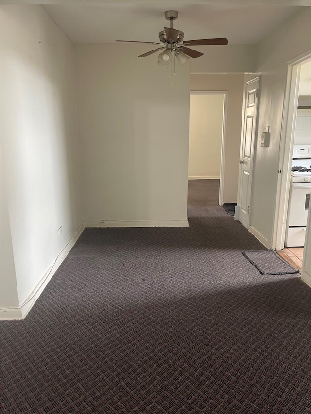 empty room with baseboards, dark colored carpet, and ceiling fan