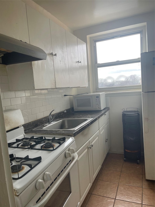 kitchen with white appliances, a sink, under cabinet range hood, dark countertops, and backsplash