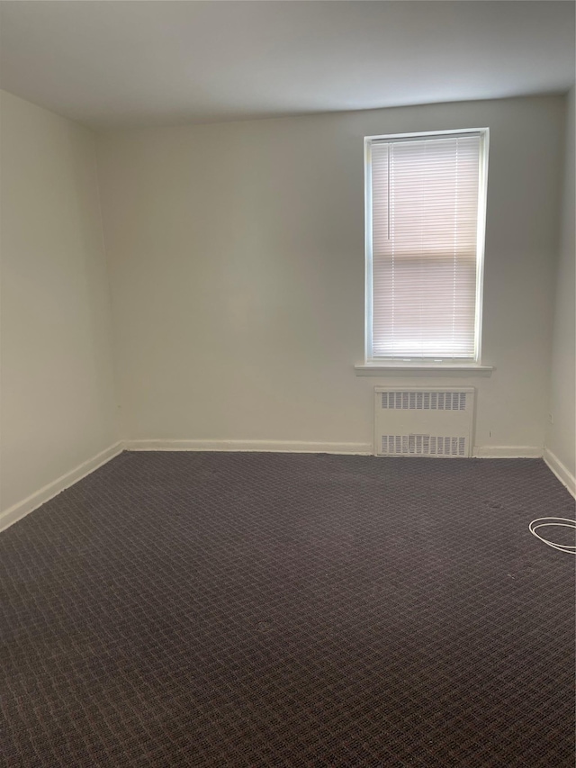 unfurnished room with baseboards, radiator, and dark carpet